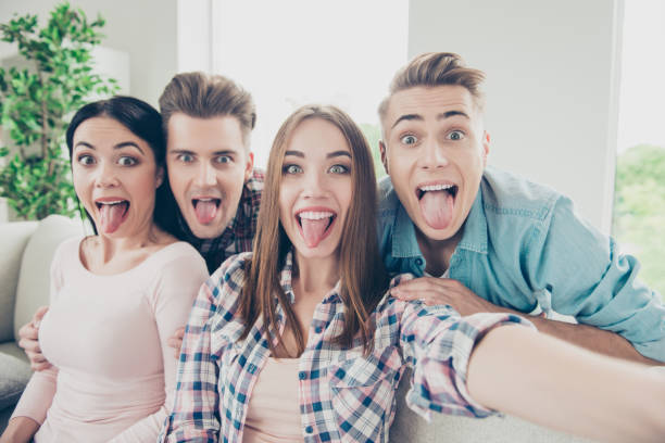 istock Cute, expression, glad hipsters in stylish casual wear take selfie on the front camera modern smartphone show tongue out 1056212718