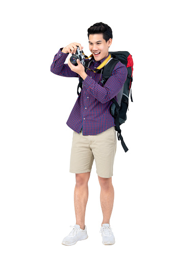 Isolated Portrait of happy young attractive asian tourist man in casual attire carrying a backpack taking a photo with his camera