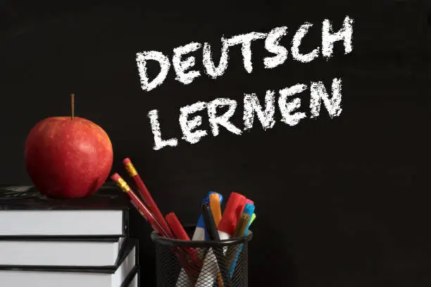 Photo of Schoolbooks, apple and chalkboard with the slogan German learning