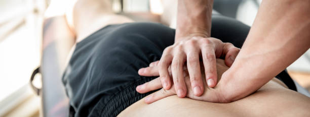 Therapist giving lower back sports massage to athlete male patient Therapist giving lower back sports massage to athlete male patient in clinic chiropractic adjustment photos stock pictures, royalty-free photos & images