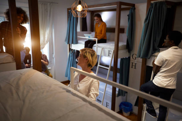 Friends In A Hostel Young travelers in hostel bedroom. Some of them sitting and resting, others climbing on ladders on bunkbed. dorm room photos stock pictures, royalty-free photos & images