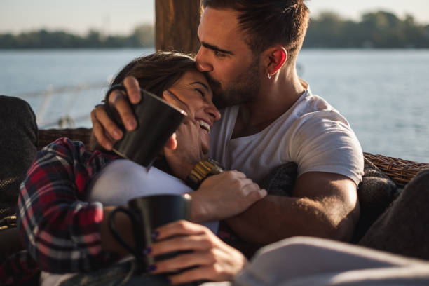 chłopak całuje swoją uśmiechniętą dziewczynę w czoło nad rzeką - love romance couple sensuality zdjęcia i obrazy z banku zdjęć