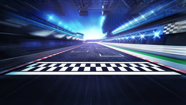 A red race car finishes first at a track while checkered flags wave. The other cars follow closely behind. The event takes place during a bright day. Spectators are in the background.