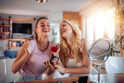 Two happy girls applying make up at home,having fun together.