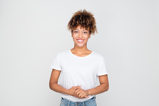 Portrait of casual afro american woman standing relaxed against grey background. Horizontal shot of african female model in t-shirt and jeans looking at camera and smiling.