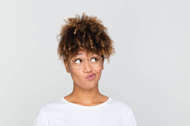 African woman making at decision Close up portrait of doubtful afro american woman looking away and making a decision on grey background grimacing stock pictures, royalty-free photos & images