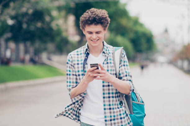 istock Curly haired cute attractive guy wearing casual walking outside smiling typing sms in smartphone 1056247808