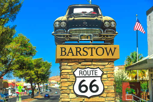 Barstow, California, USA - August 15, 2018: Barstow Sign with 1961 Corvette Convertible along Route 66. Barstow is located in Mojave Desert, san Bernardino County. American flag on background