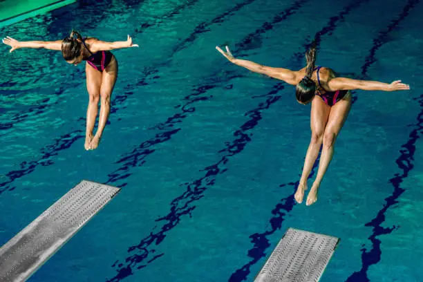 Two female divers diving into the pool. Tandem diving