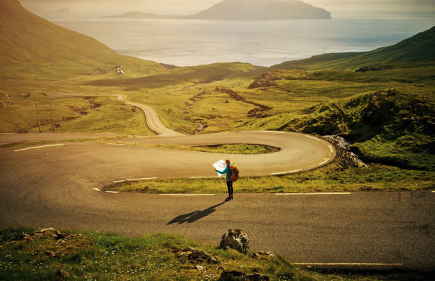 I think this is the right place Shot of a carefree young woman standing in the middle of a road while reading a map to her next destination outside in nature faroe islands photos stock pictures, royalty-free photos & images