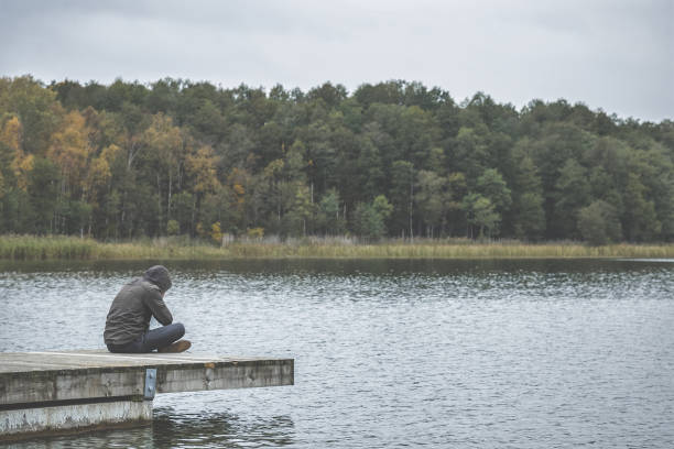 istock Young man sitting on footbridge at lake. Suffering from life difficulties, broken heart or psychological problems. Dark, gloomy thoughts. Social isolation. Cool nature landscape in autumn time. 1056257576
