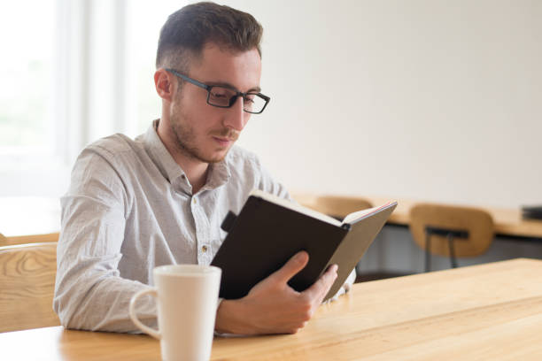 istock Serious male student reading textbook at table in cafe 1056263656