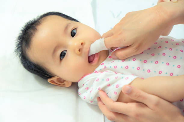 母は、清潔なガーゼでアジアの赤ちゃん舌をきれいにするのに指を使用します。 - finger in mouth ストックフォトと画像