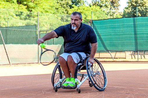 disabled tennis player hits the ball backhand during a match outdoor