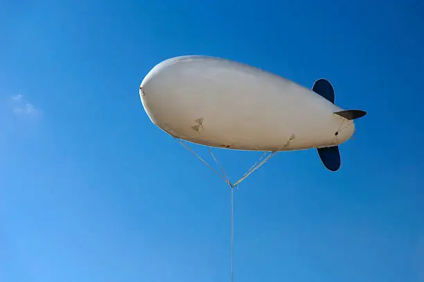White inflatable airship hovering in blue clear sky