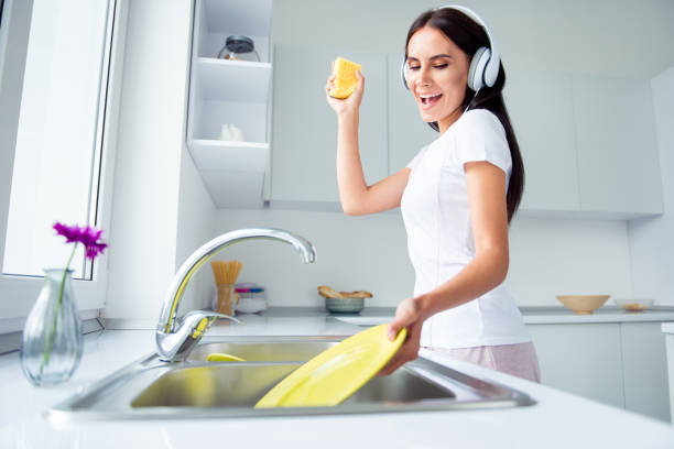adorable attractive young brunette smiling woman wearing pajama, washing dishes, listening to music, singing in light kitchen - spring cleaning women cleaning dancing imagens e fotografias de stock