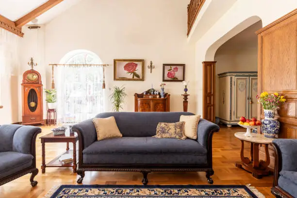 Cobalt blue sofa and other antique furniture on a wooden floor in a spacious living room interior of a classic mansion.