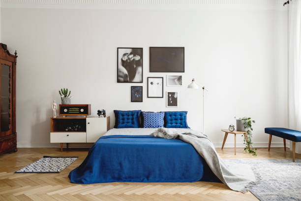 istock Vintage bedroom interior with bedside table, king size bed with blue bedding and pillows. Mockup gallery on the white wall. Real photo concept 1056285298