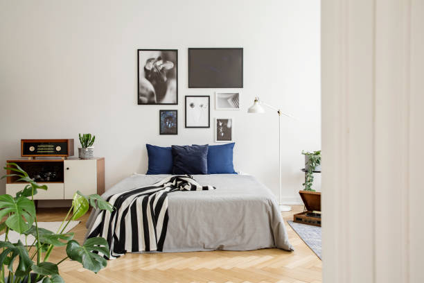 белый деревянный комод рядом с кроватью с темно-синими подушками, серым одеялом и полосатым черно-белым одеялом в спальне с обрамленной худ - poster bed audio стоковые фото и изображения