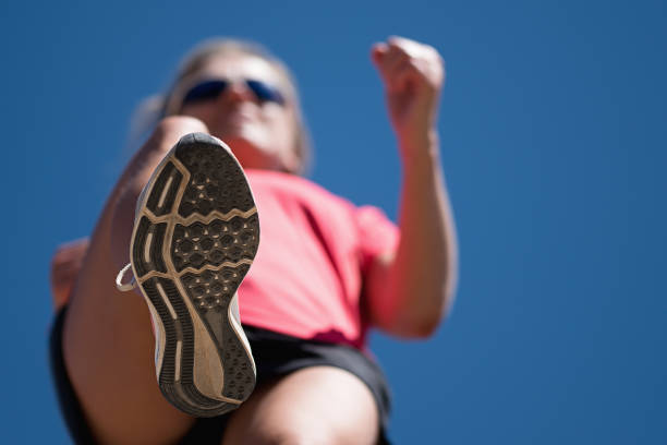 A person running outdoors on a sunny day. Only the feet are visible. The person is wearing black running shoes.Exercise, fitness and healthy lifestyle.
