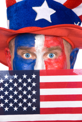 A patriotic man with red, white and blue face paint holds up an American flag.