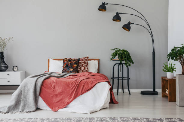 istock Black stylish lamp in elegant bedroom interior with comfortable double bed, plants, and bedside table, real photo with copy space on the wall 1056289120