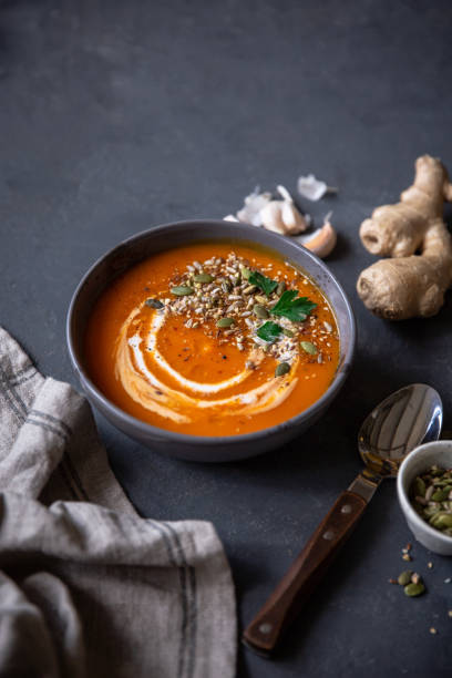 Fresh orange winter squash cream soup in bowl on dark grey table. Healthy dinner with pumpkin soup and cream. Serving with ginger and pumpkin seeds. squash soup stock pictures, royalty-free photos & images