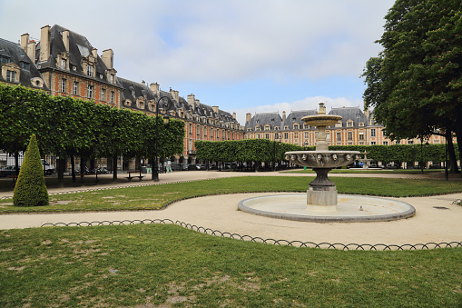 Place des Vosges with renaissance buildings and park and fountain in Paris, France