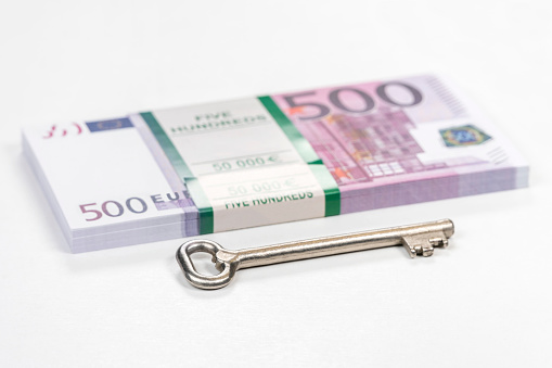 large metal house key next to a bundle of money with a face value of five hundred euro