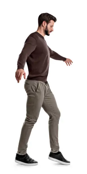 A fit man in casual clothes looks down as he lifts his foot during tightrope walking steps on a white background. Party tricks. Risk and gain. Danger of falling.