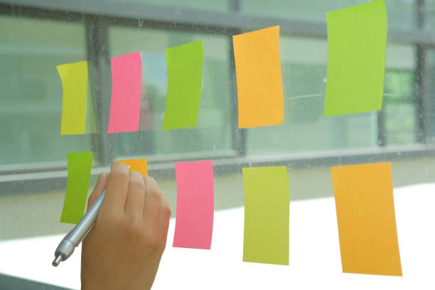 istock hand write on adhesive notes on glass wall. Sticky note paper reminder schedule for discussing creative idea & business brainstorming 1056306256