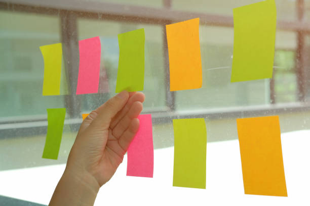 istock hand hold adhesive notes on glass wall. Sticky note paper reminder schedule for creative idea & business brainstorming 1056306258