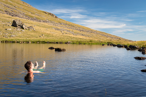 Beautiful landscape view of Greendale Tarn in the Lake District National Park, UK. A man relaxing and enjoying refreshing bath in cold tarn water on a beautiful sunny day.