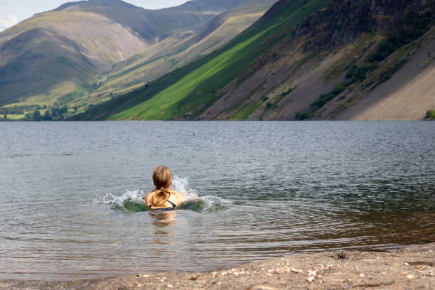 Beautiful landscape view of Wast Water in the Lake District National Park in the UK. A girl relaxing and enjoying refreshing bath in cold water on a beautiful sunny day. stock photo