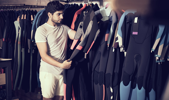 Adult european man holding and choosing suit for surfing in the shop