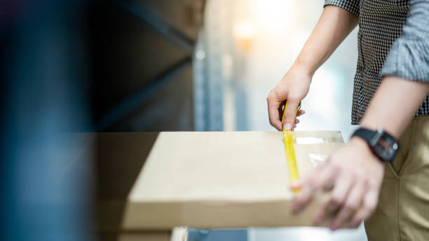 Male worker hand using tape measure for measuring dimension of product in cardboard box. Shopping lifestyle in warehouse concept stock photo
