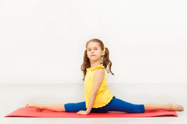 Side view portrait of seven years old girl performing front split during gymnastic lesson