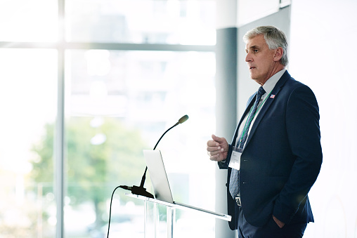 Mature businessman speaking in microphone and presenting his report at conference