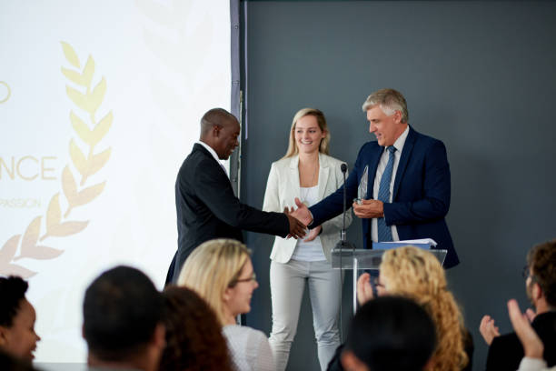 Well done on this great achievement Shot of a young businessman being awarded a prize during an awards giving ceremony at a conference receiving stock pictures, royalty-free photos & images