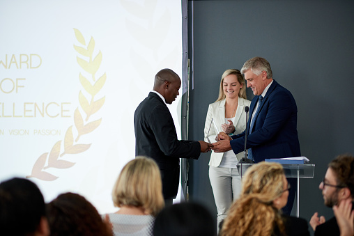 Shot of a young businessman being awarded a prize during an awards giving ceremony at a conference