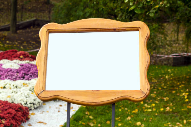 istock Mockup with empty white square signboard tablet in curly wooden frame against the background of bright flower bed of colorful chrysanthemums and green grass. Empty sign, nameplate, plate in the park, garden 1056367456