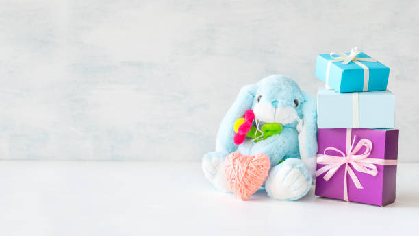 istock Cute toy soft blue bunny with a flower and pink thread heart with soap bubbles on light background. Birthday card, Valentine's Day, mother's day, gift present background. 1056372232