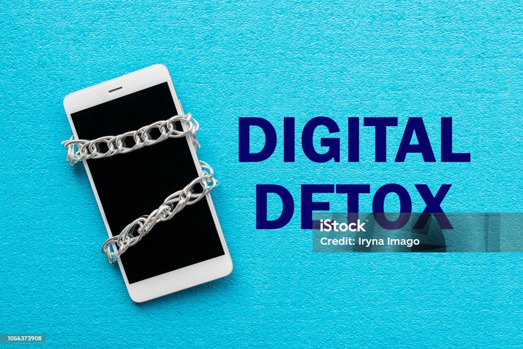 White smartphone with metal chain on blue background. Digital detox, dependency on tech, no gadget and devices concept Digital Detox Stock Photo