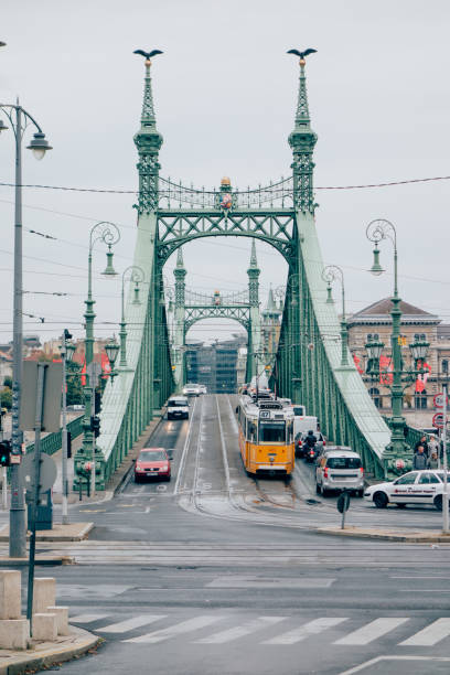 Budapest, Hungary - October 2, 2018: Liberty bridge with streets and cable car and people walking around, cloudy sky, day light.