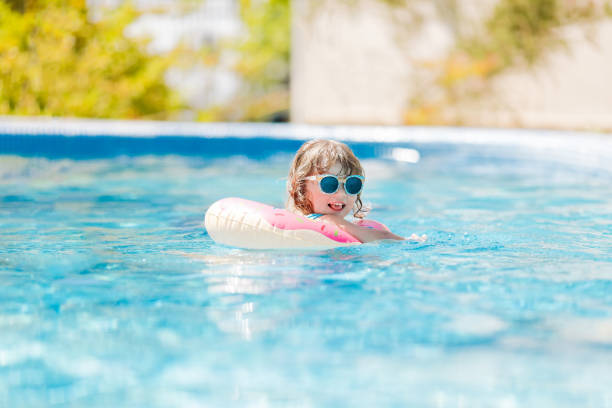 Little girl in swimming pool on funny inflatable donut float ring, learning how to swim.