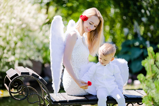 Beautiful mother and her toddler son wearing angel costumes. Cheerful moment, loving family. Mom is the Guardian angel for her child concept.