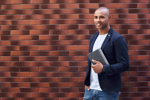 istock Brain development. Young guy standing on wall holding book looking aside smiling cheerful 1056395002