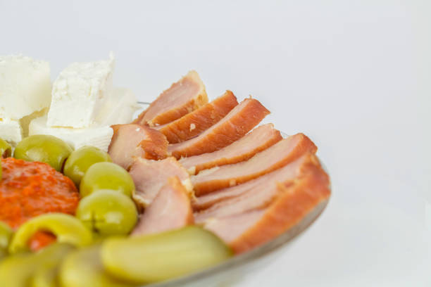 Plate of various appetizers including smoked meat, cheese, olives, pickles and pepper spread, isolated on white.
