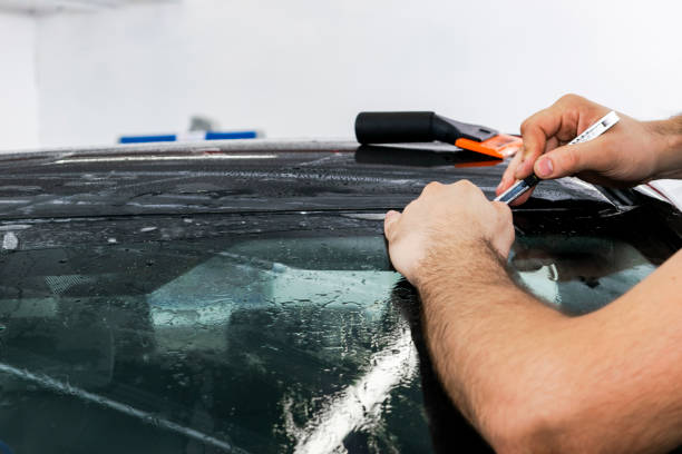 Car wrapping specialist putting vinyl foil or film on car. Protective film. Applying a protective film with tools for work. Car detailing. Transparent film. Car paint protection. Trimming. especialista en coches envoltura poner papel vinilo o película en el coche. película protectora. aplicar una película protectora con herramientas para el trabajo. detalle de coche. película transparente. protección de la pintura del coche. recorte.