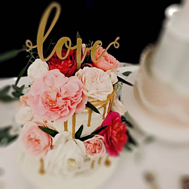 Wedding cake Wedding cake with fresh seasonal flowers, dripping gold icing and a gold cake topper with the word love. wedding cake close up macro stock pictures, royalty-free photos & images